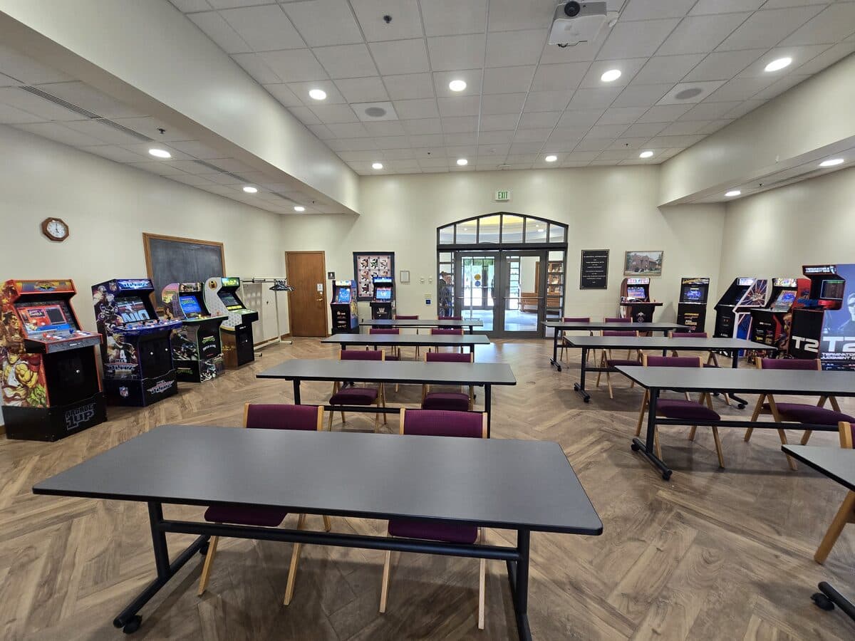 Row of classic arcade cabinets set up among tables and chairs in the North Manchester Public Library meeting room